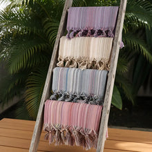 A set of colorful turkish beach towels with soft pastel stripes tassels and fringed edges displayed on a wooden ladder