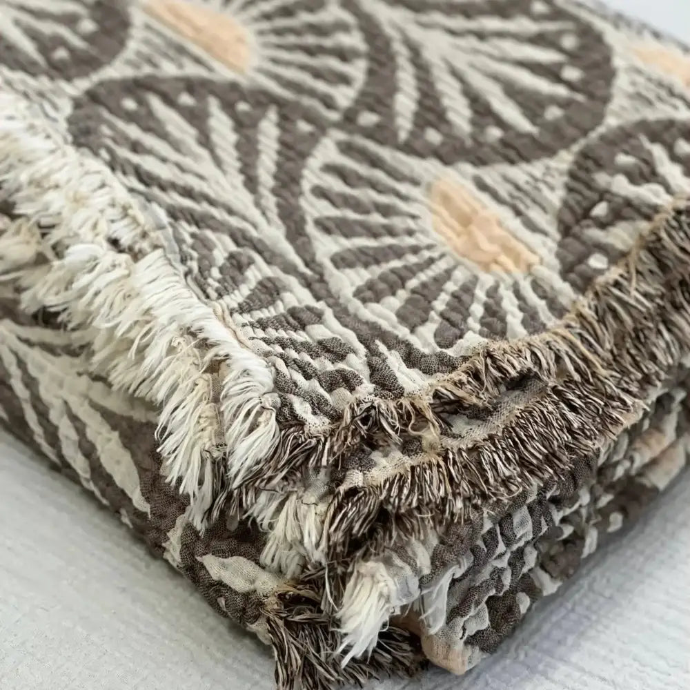 Soft muslin bed blanket with ginko design and fringe edges in gray, white, and peach