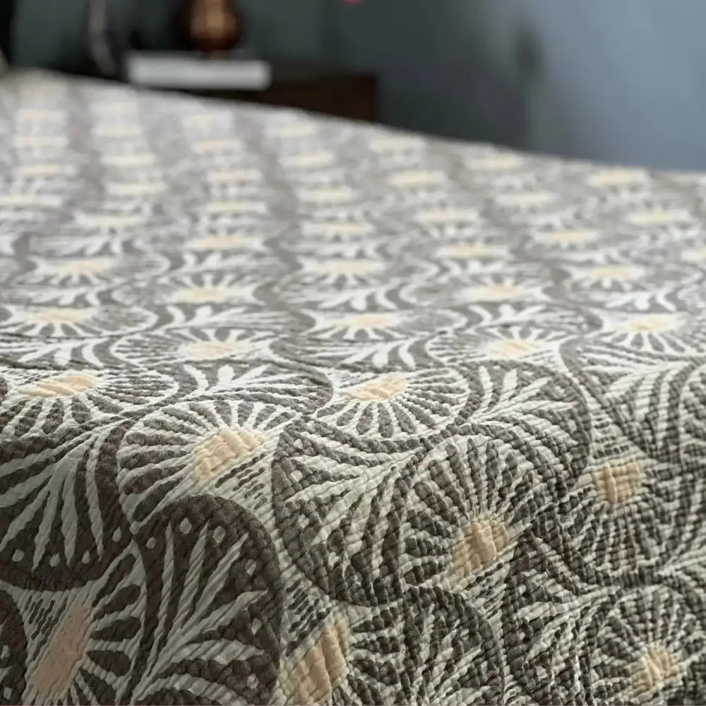 A muslin bed blanket with ginko design featuring a circular fan pattern in grey and off-white
