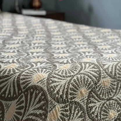 A muslin bed blanket with ginko design featuring a circular fan pattern in grey and off-white