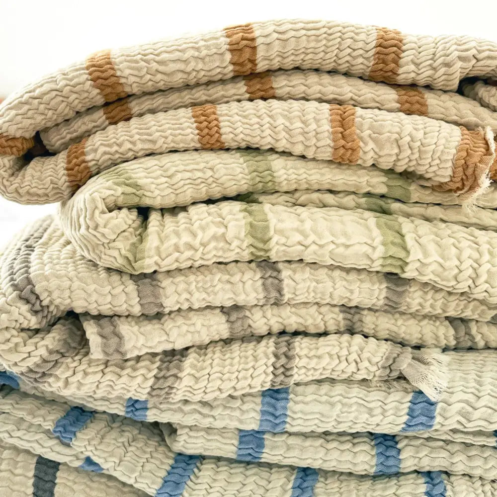 Stack of reversible muslin bed blankets with stripes in varying colors.