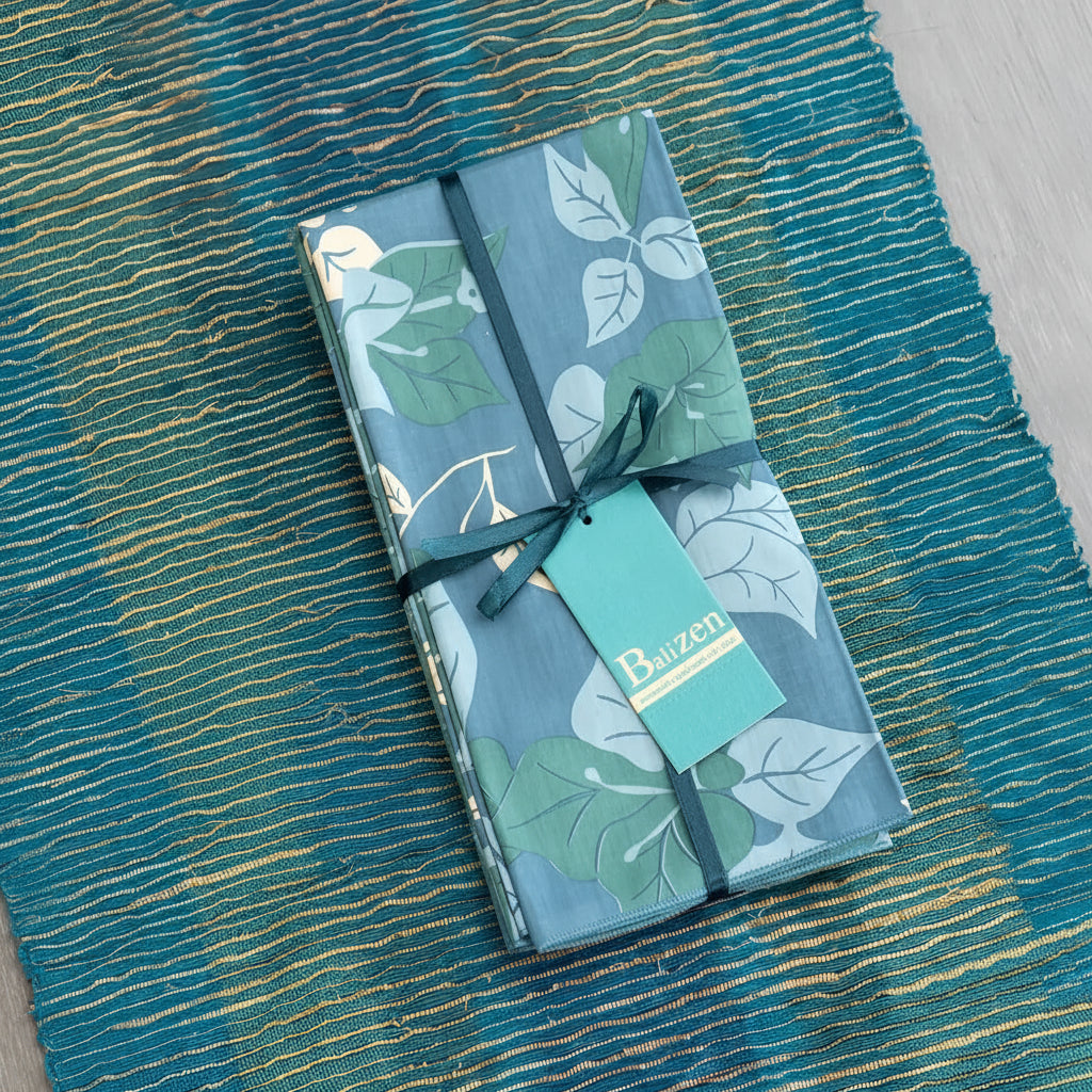 Set of 4 handmade blue and gree leaf-patterned napkins wrapped in dark green ribbon on a vetiver table runner with baizen tags