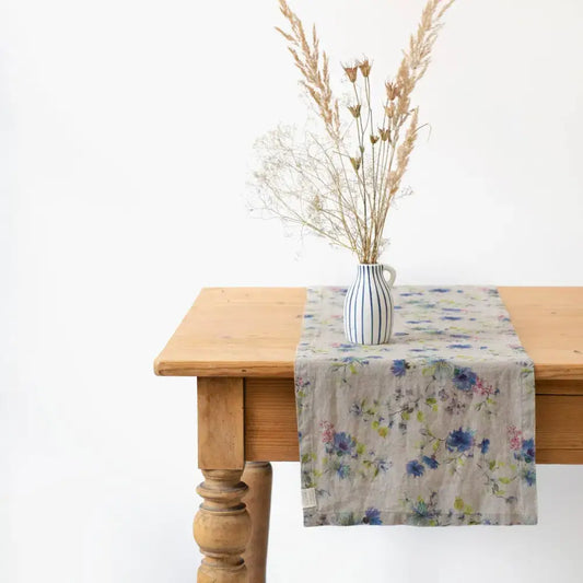 Table runner with floral design on wooden table with a vase of flowers.