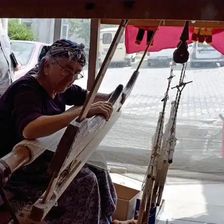 An older woman operating a traditional weaving loom.