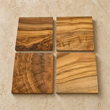 Four square coasters handcrafted from olive wood with unique natural grain patterns in warm golden and brown tones