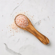 A 3.5 inch olive wood salt spoon filled with pink himalayan salt crystals for spices and condiments use