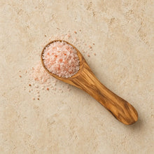 A 3.5 inch olive wood salt spoon filled with pink himalayan salt crystals perfect for spices and condiments