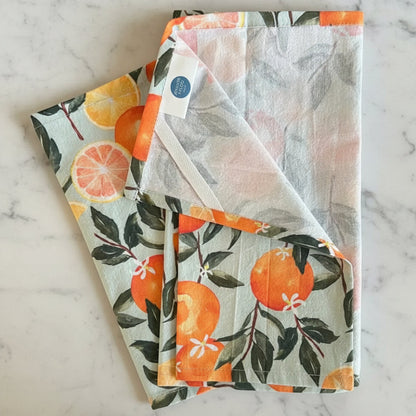 A handmade pure cotton tea towel in light gray with a vibrant orange citrus print perfect for kitchen decor