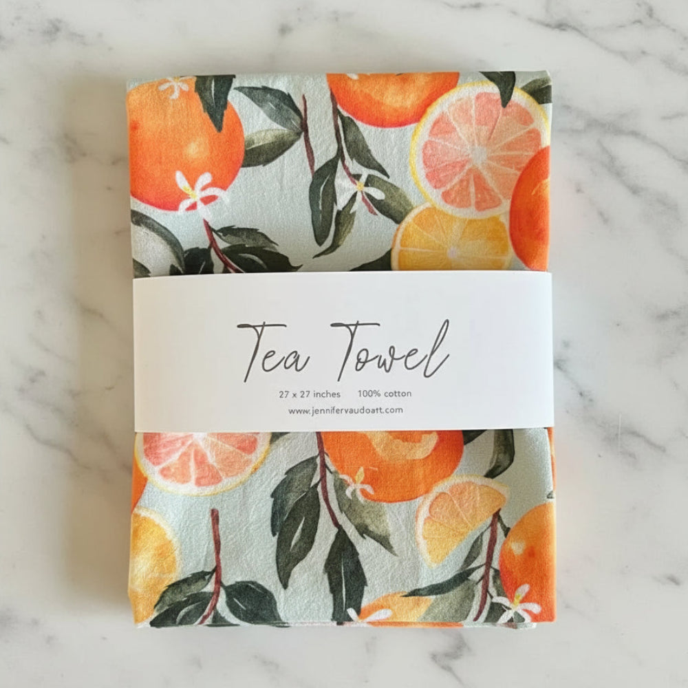 Folded pure cotton handmade tea towel with vibrant orange watercolor print and green leaves on light gray background