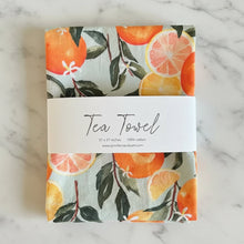 Folded pure cotton handmade tea towel with vibrant orange watercolor print and green leaves on light gray background