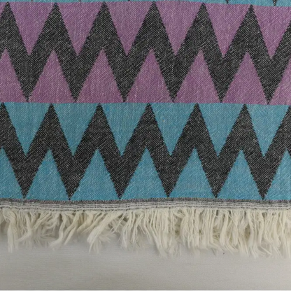 A vibrant purple and teal organic bath towel with zigzag pattern and fringed edge perfect for beach use