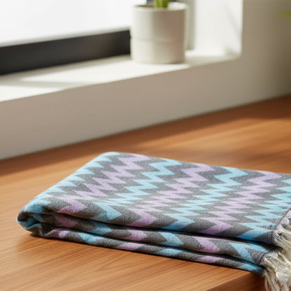 Folded organic bath towel with bold purple and light blue zigzag pattern and white fringed edges for beach use