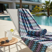 A rolled organic bath towel with a bold purple blue gray zigzag pattern and white fringe perfect for beach use