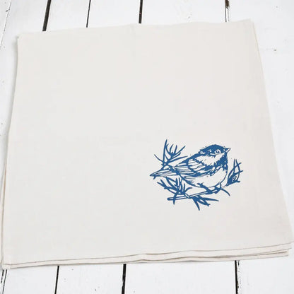 A white cloth napkin, hand-printed with an original Chickadee design in navy blue. 