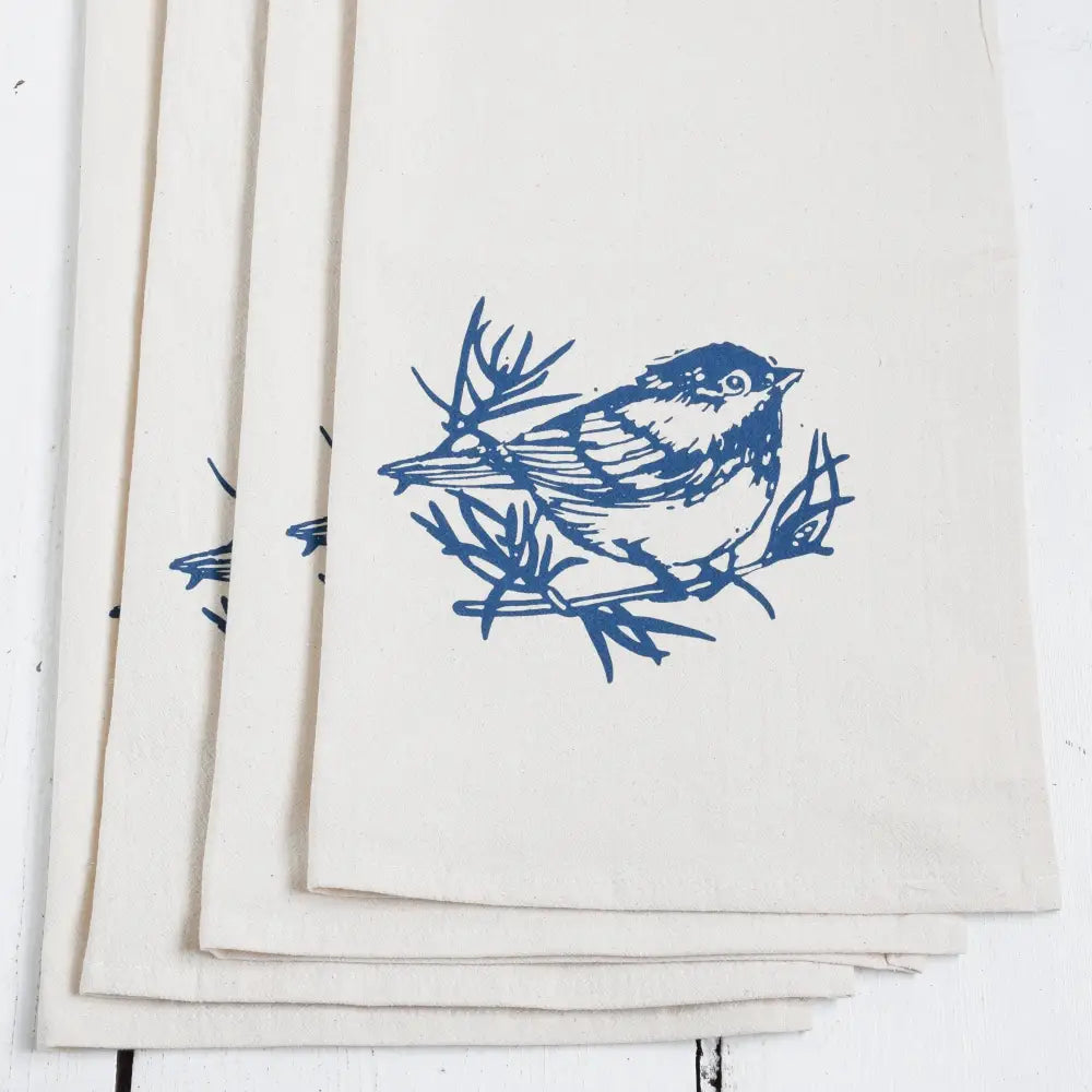 A white cloth napkin, hand-printed with an original Chickadee design in navy blue. 