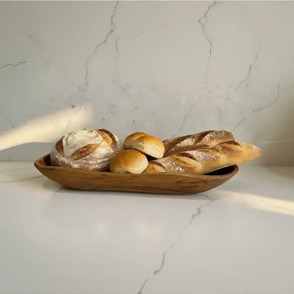 A rustic salvaged teak root wooden oval bread bowl holding assorted freshly baked loaves and rolls