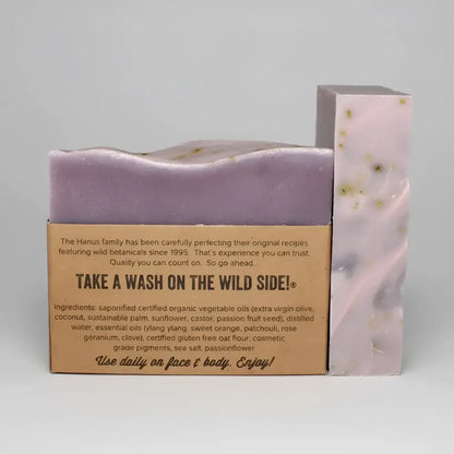 Purple handmade passionflower bar soap with speckled green flecks wrapped in kraft paper featuring ylang ylang and passion fruit seed
