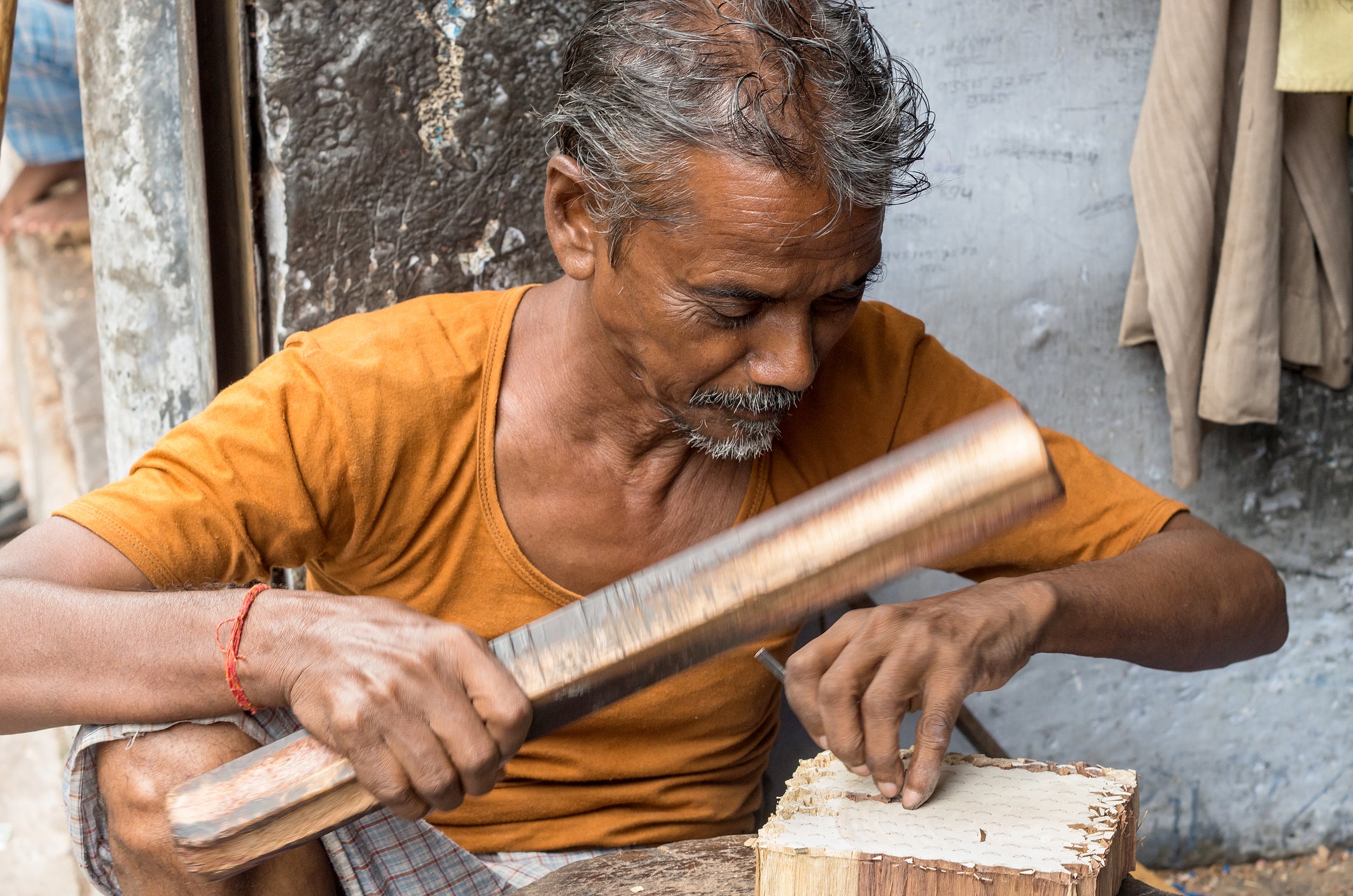 Man working with a large tool on a wooden block in an outdoor setting