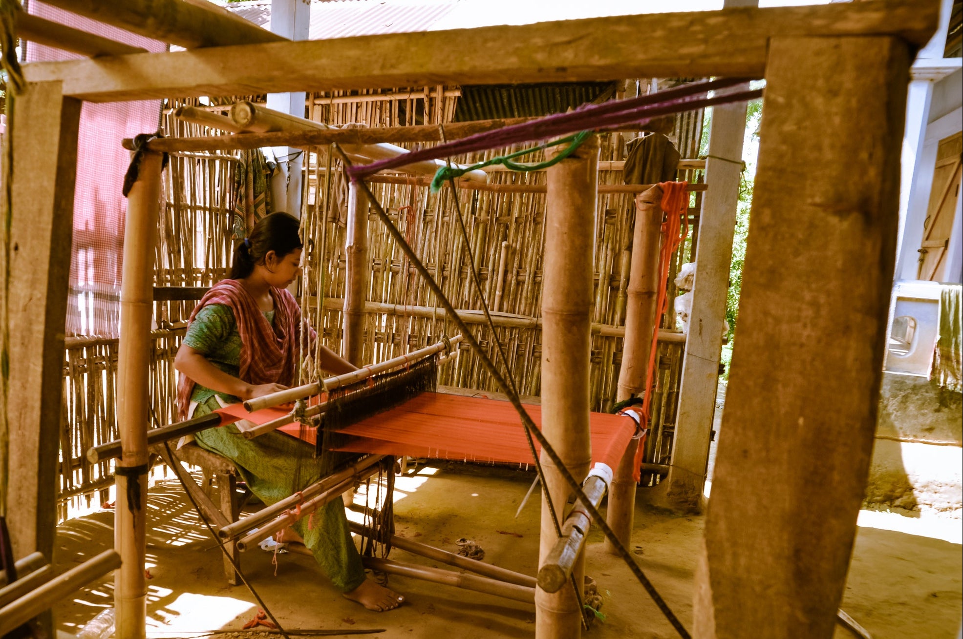 Woman weaving on a traditional loom in a rustic setting