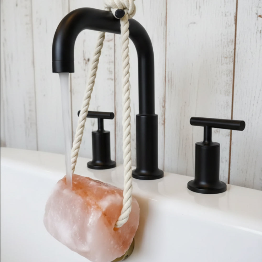 Pink Himalayan salt rock suspended by white rope from black faucet