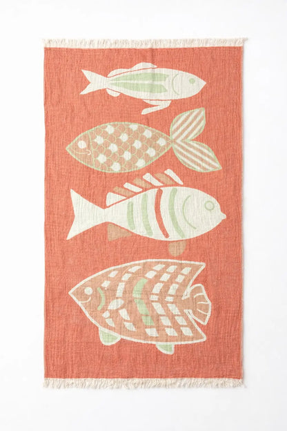 Coral-colored turkish cotton beach towel with four white and light green fish patterns and fringed edges perfect as a beach blanket