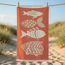 A coral-colored premium authentic turkish cotton muslin beach towel with fringed edge and fish design hanging on a line
