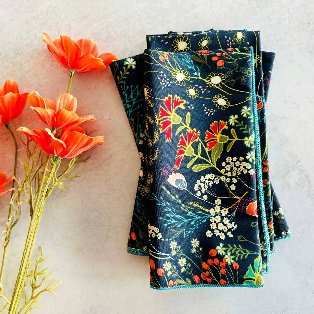 Folded dark pretty peacock cloth napkins with colorful floral pattern and teal edging