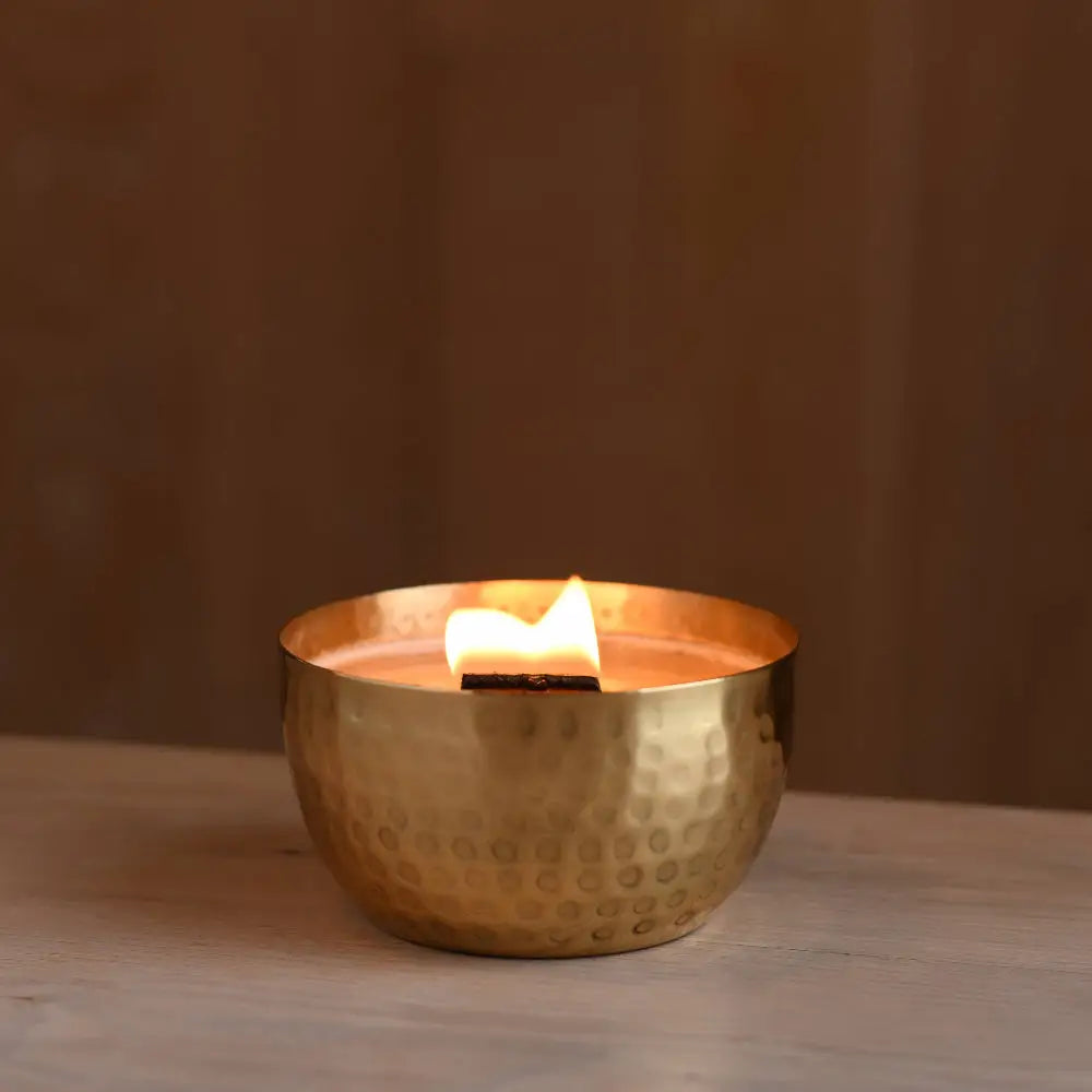 Lit soy candle with wooden wick in a hammered solid brass bowl with crushed thyme herb
