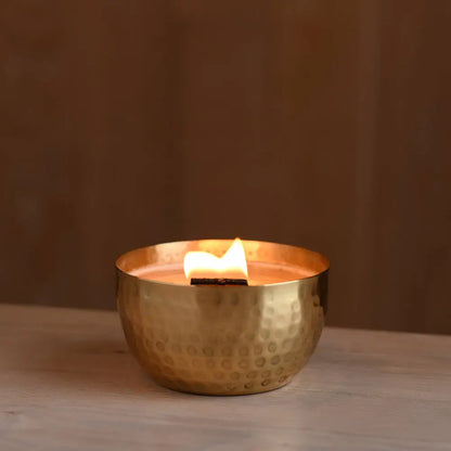 Lit soy candle with wooden wick in a hammered solid brass bowl with crushed thyme herb