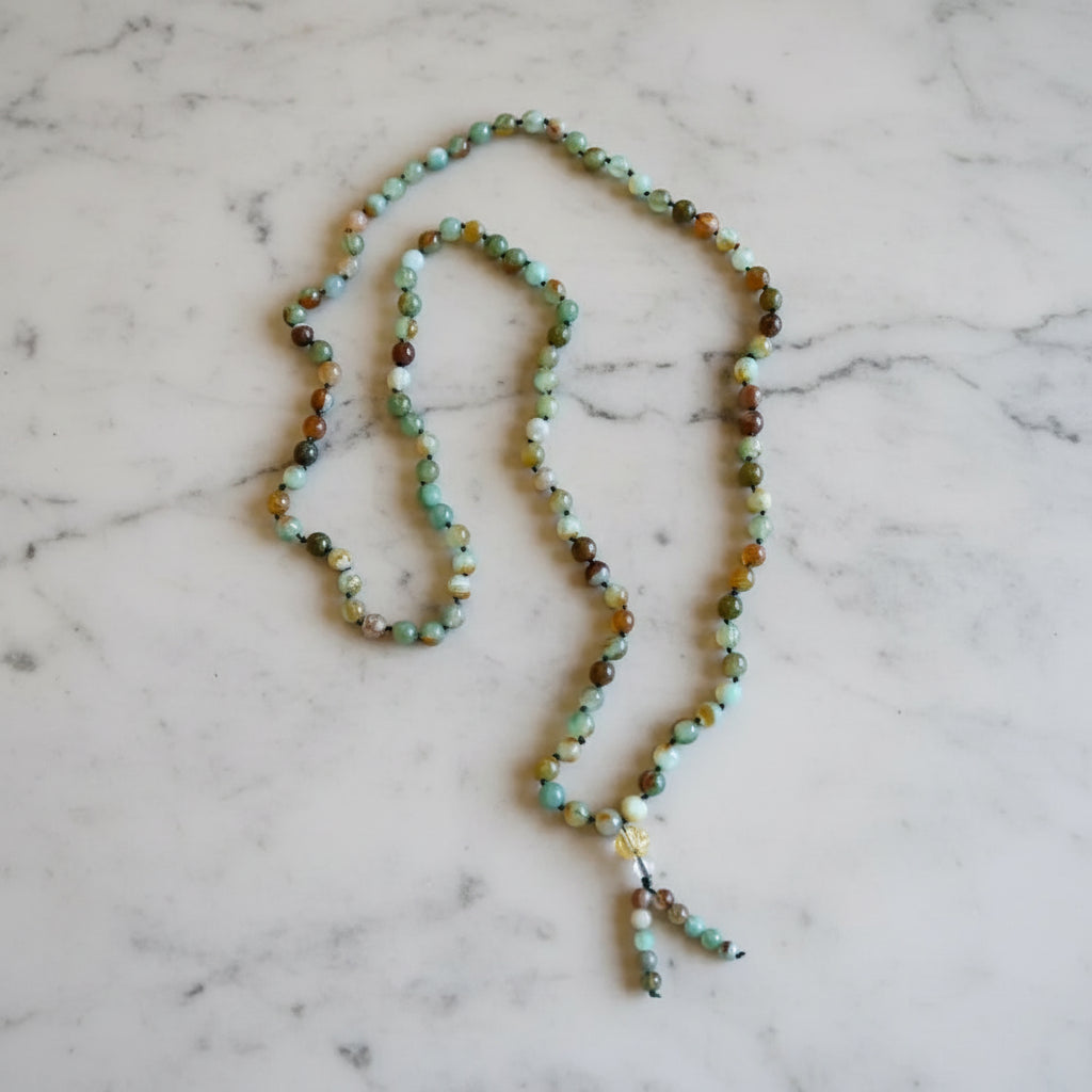 A rainbow agate mala necklace with smooth green brown and cream rainbow agate beads and a beaded tassel