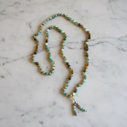 A rainbow agate mala necklace with smooth green brown and cream rainbow agate beads and a beaded tassel