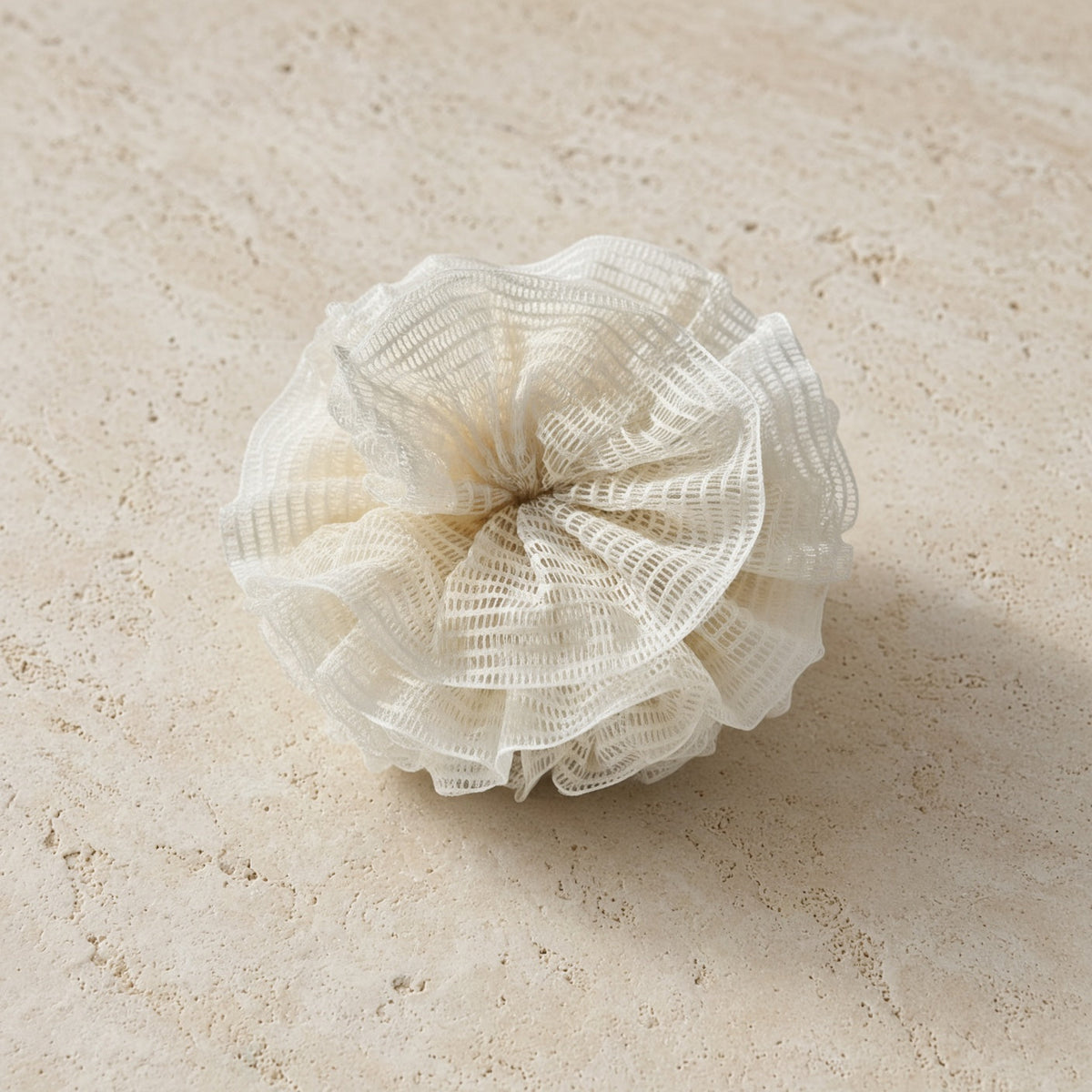 A delicate off-white ramie shower pouf with ruffled mesh and layered folds for a natural exfoliation experience using pure ramie plant fibers