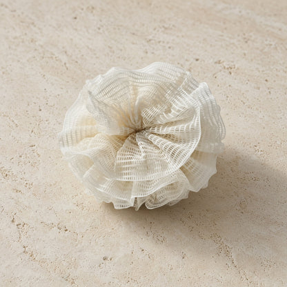 A delicate off-white ramie shower pouf with ruffled mesh and layered folds for a natural exfoliation experience using pure ramie plant fibers