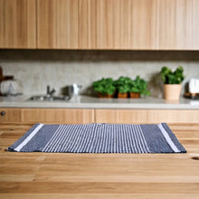 A woven navy blue and white striped recycled cotton placemat made from leftover fabric on a wooden countertop