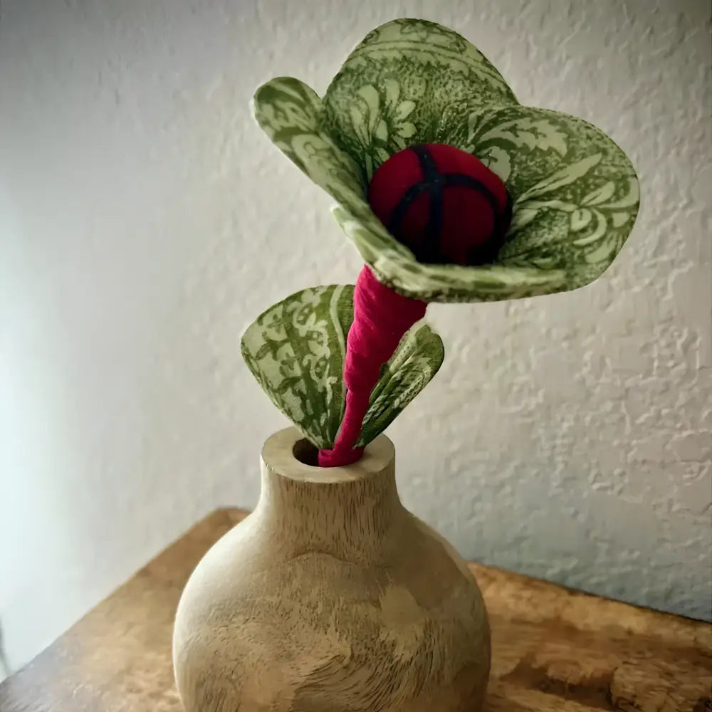 Decorative vase with a green and red floral arrangement on a wooden surface.
