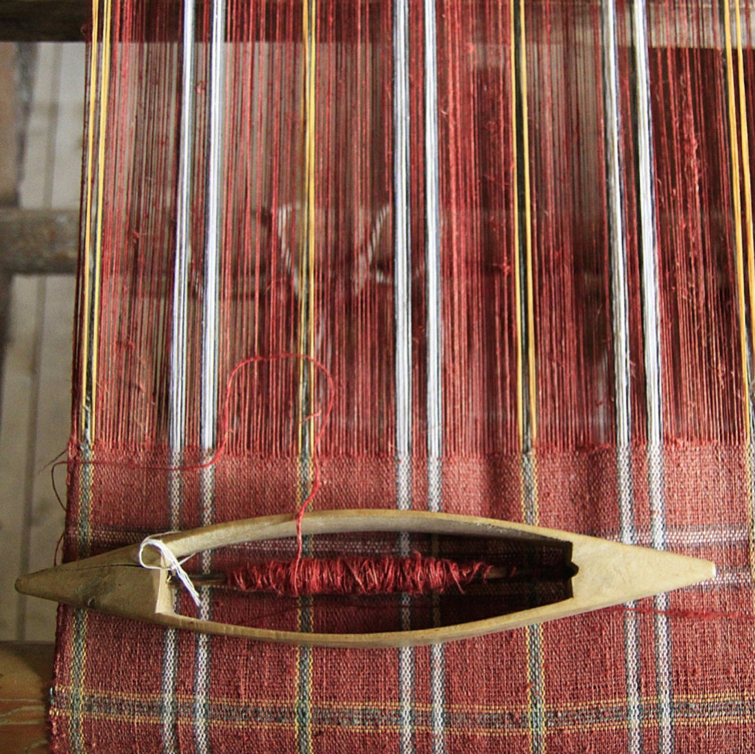 Weaving loom with red and gold threads on a wooden frame