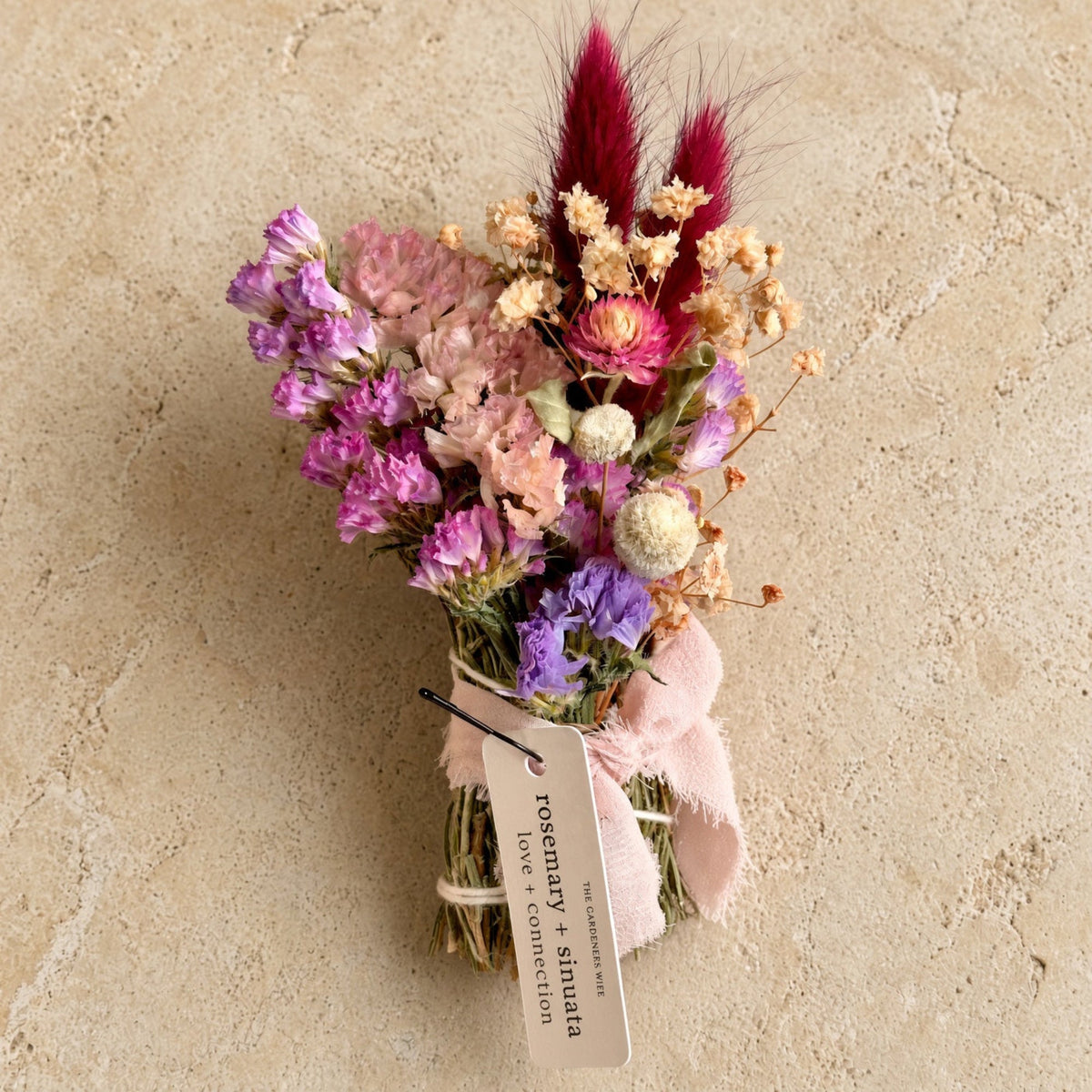 A sinuata smudge stick featuring a bouquet of dried purples pinks and cream flowers with red grasses honoring relationships