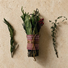 A bundle of dried rosemary thyme and bay leaf smudge tied with twine and wrapped in maroon paper for smoke rituals and purifying energy