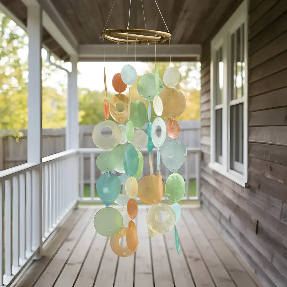 A colorful round capiz chime with translucent orange blue and green circular pieces hanging from a bamboo hoop