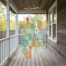 A colorful round capiz chime with translucent orange blue and green circular pieces hanging from a bamboo hoop
