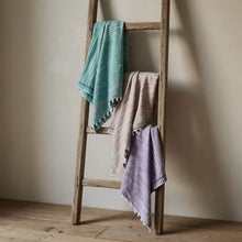 Three handloomed organic cotton towels in teal beige lavender hang on a rustic ladder showing rustic texture