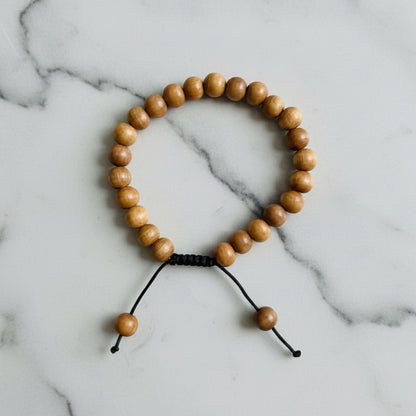 A sandalwood mala bracelet made of warm natural wood beads with a simple black cord closure