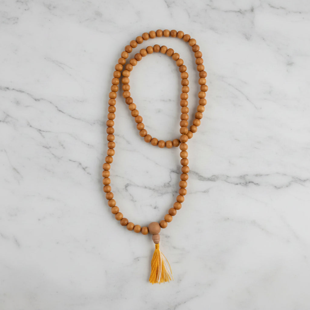 A sandalwood mala with 8 mm natural-toned wooden beads and a small cotton tassel made from sustainably sourced wood