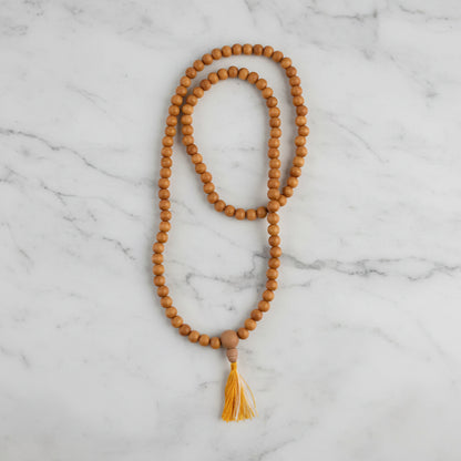 A sandalwood mala with 8 mm natural-toned wooden beads and a small cotton tassel made from sustainably sourced wood