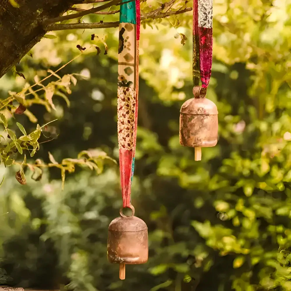 A pair of copper bells anging in a tree with colorful ribbons