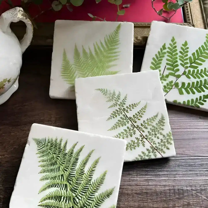 Stone coasters with fern design on a wooden surface.
