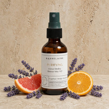 Brown glass shower spray mist with dark green nozzle labeled baudelaire purifying vibrant citrus medley 2oz surrounded by citrus slices and lavender