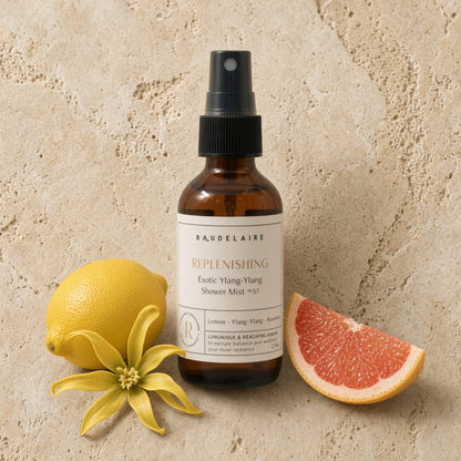 A sleek amber glass shower spray mist with exotic ylang-ylang scent beside citrus fruits and a yellow flower