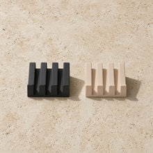 Black and beige silicone soap dish with integrated self-drainage and slanted slot design featuring vertical ridges