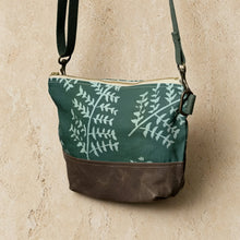 Small teal crossbody bag with artisan-designed fern pattern and brown leather bottom featuring waxed canvas durability